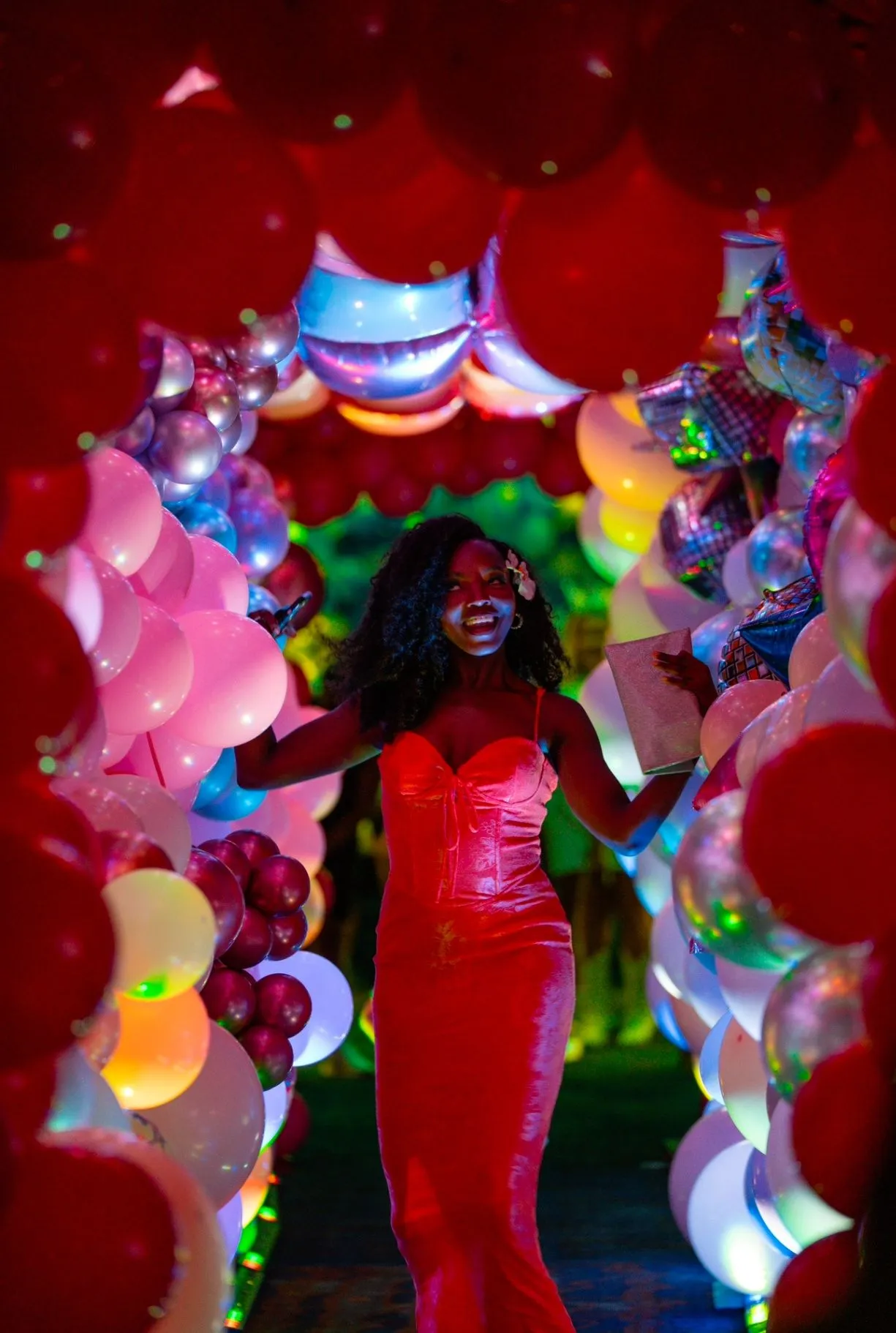 Guest in a red dress walking through a colorful balloon tunnel under vivid event lighting