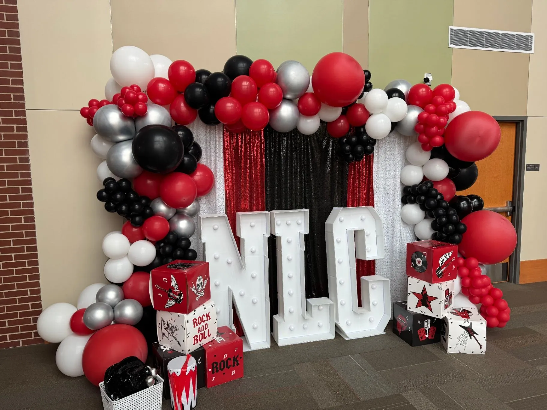 NLC light-up marquee letters framed by a red, black, and silver balloon arch with themed decor boxes