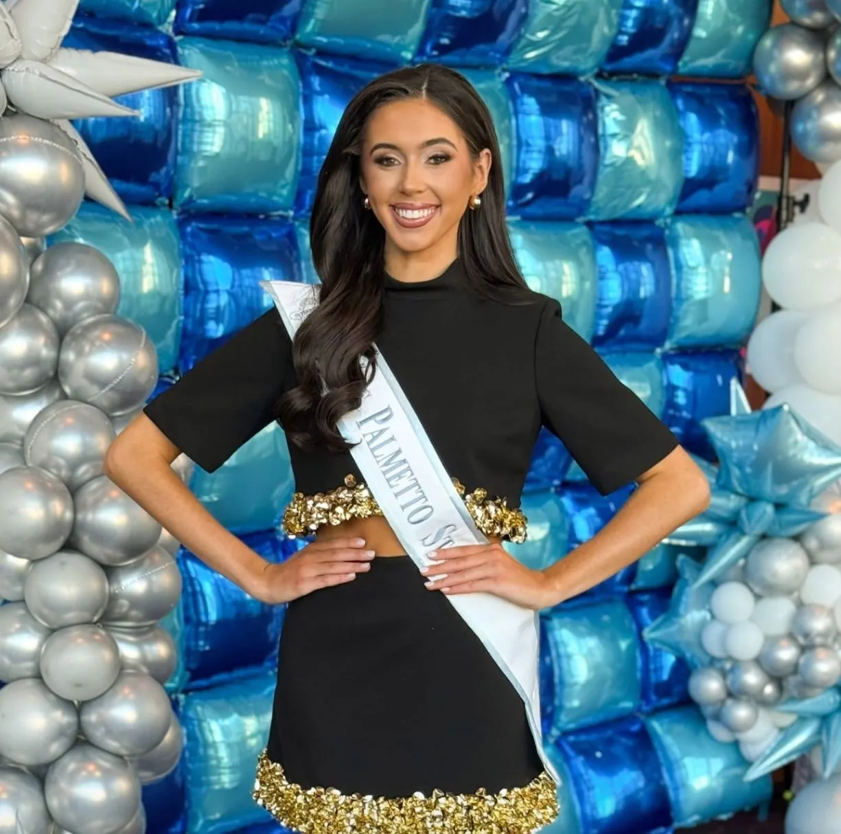 Titleholder posing in front of a blue and silver metallic balloon wall with star balloon accents