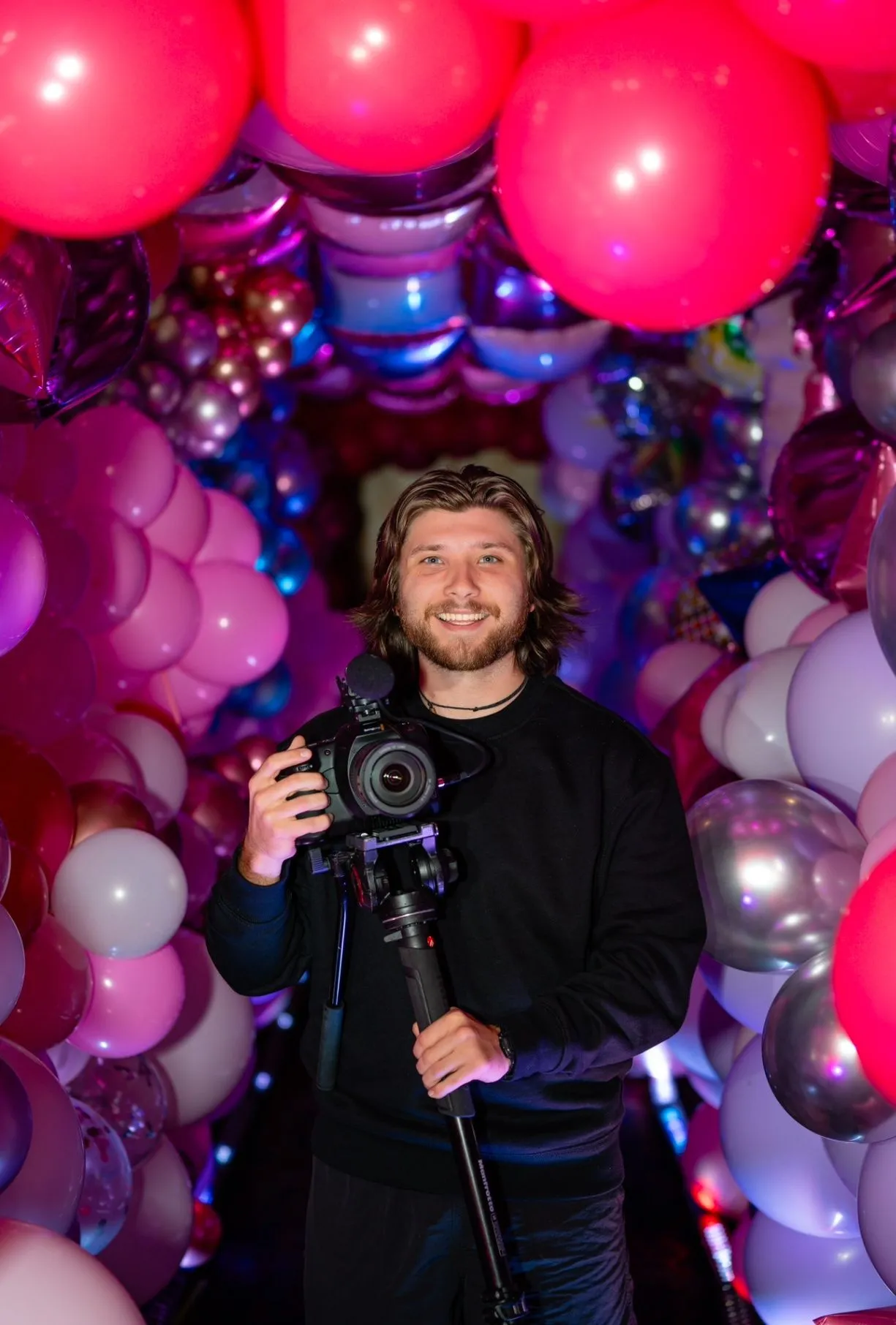 Camera operator holding a camera inside a pink-and-purple balloon tunnel