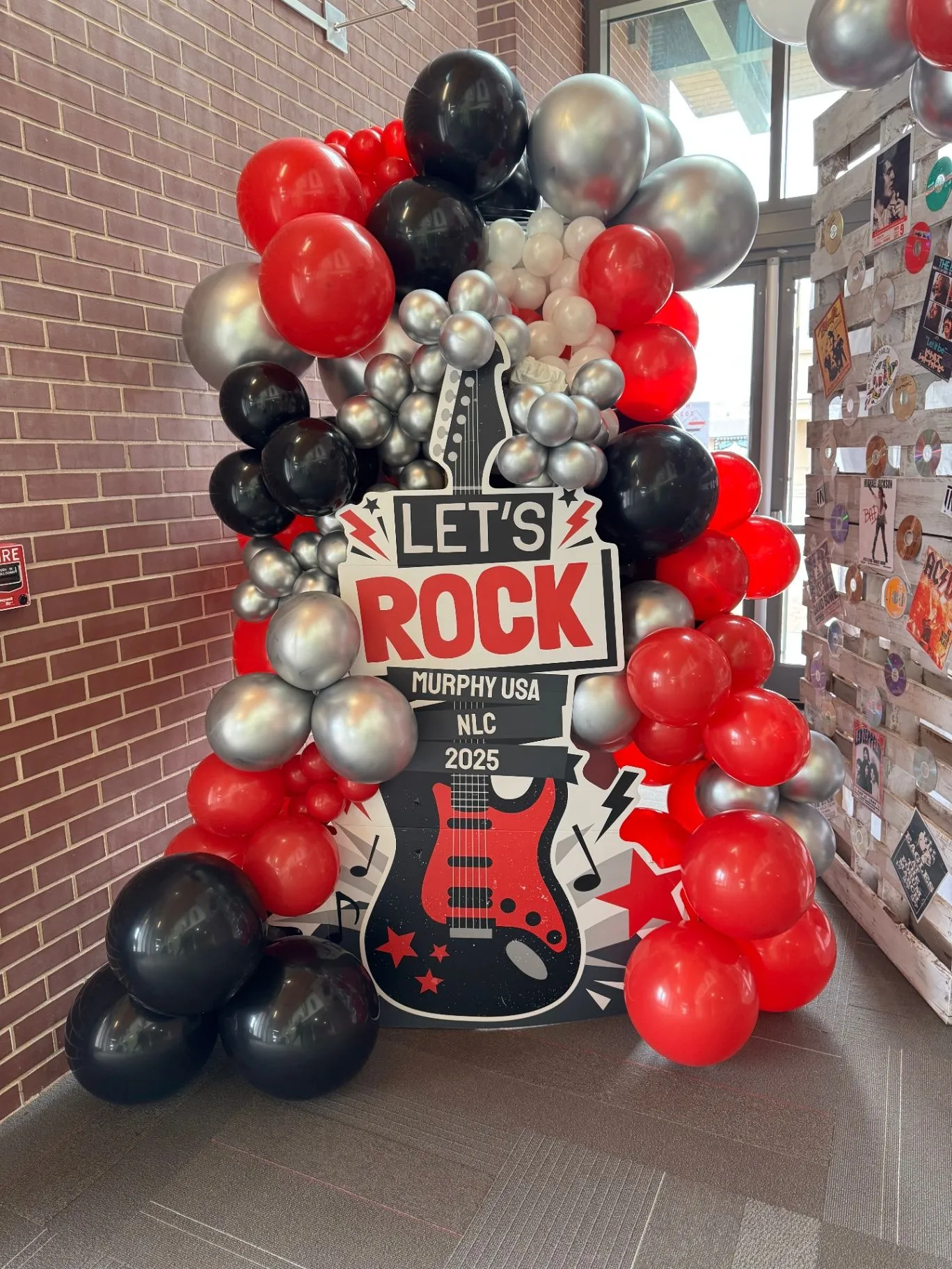 Vinyl-record and concert-poster pallet photo wall with red, black, and silver balloon garland